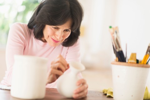 Senior woman painting handmade pottery.