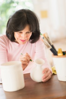 Senior woman painting handmade pottery.