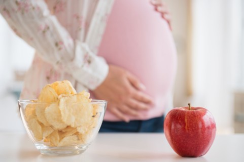 Pregnant woman choosing between apple and chips