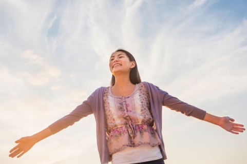 Upward view of teenage girl ( 16-17 years) standing with arms raised