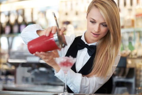 Young female bartender pouring cocktail