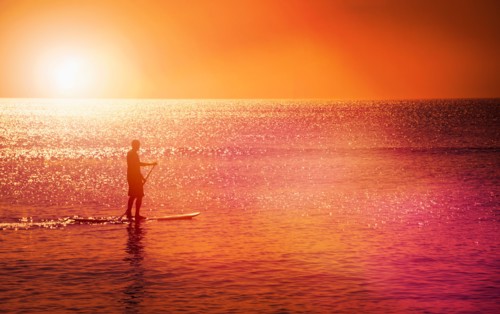 Man standing on paddle board at sunset