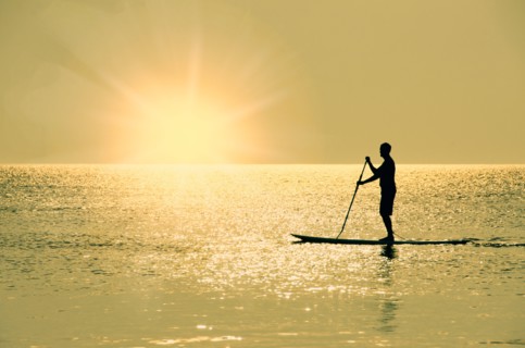 Man standing on paddle board at sunset