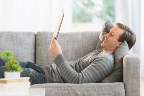 Man lying on sofa watching tablet pc.