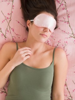 Woman with sleep mask lying on bed .