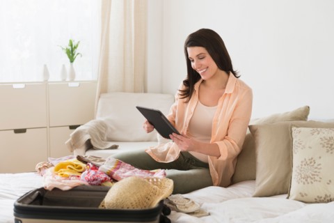 Woman using digital tablet while packing suitcase.
