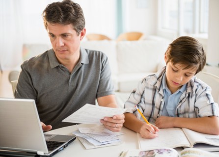 Father working on laptop and son (8-9) doing homework