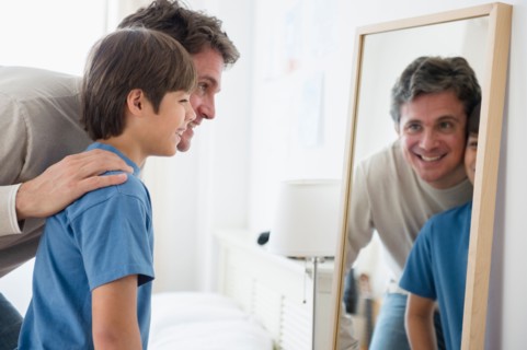 Father and son (8-9) looking into mirror