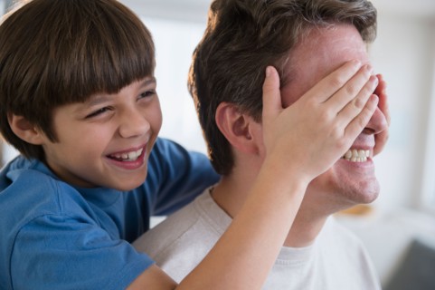 Son (8-9) covering father's eyes