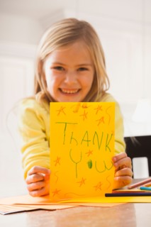 Girl (6-7) holding drawing with text 'thank you'