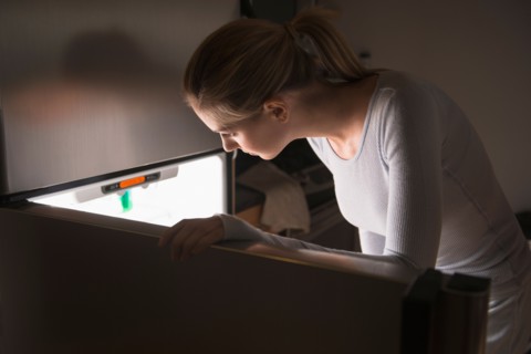 Woman opening fridge at night.