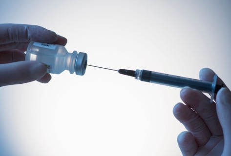 Close up of hands in surgical gloves preparing syringe for injection, studio shot.