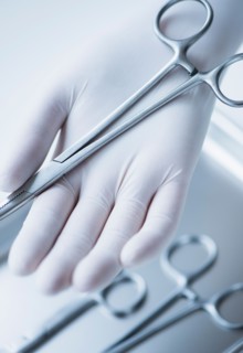 Close up of hand in surgical glove holding dental forceps, studio shot.