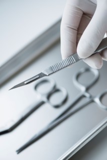 Close up of hand in surgical glove holding dental scalpel, studio shot.