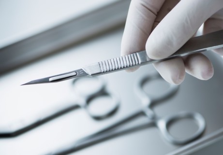 Close up of hand in surgical glove holding dental scalpel, studio shot.
