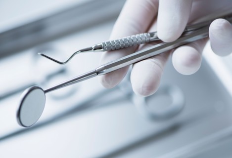 Close up of hand in surgical glove holding dental tools, studio shot.