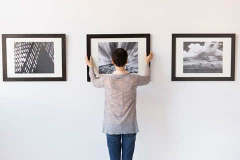 Woman hanging photographs in art gallery.