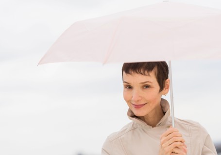 Portrait of smiling woman wearing raincoat and holding umbrella.