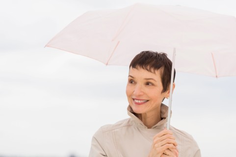 Portrait of smiling woman wearing raincoat and holding umbrella.