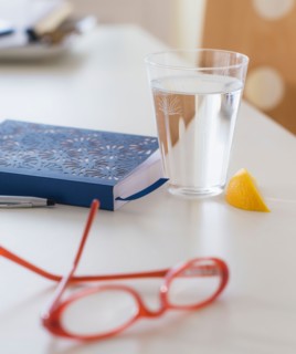 View of spectacles, personal organizer and glass of water on table
