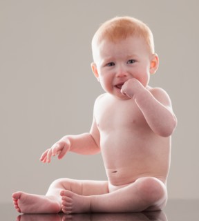 Studio shot of naked baby boy (18-23 months) with finger in mouth