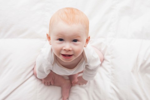 Directly above portrait of baby boy (18-23 months) sitting on duvet and looking at camera
