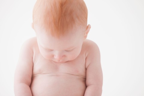 Naked baby boy (18-23 months) looking at his belly