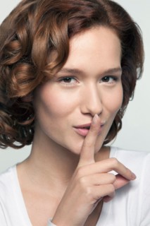 Studio shot portrait of young woman in white blouse with finger on lips