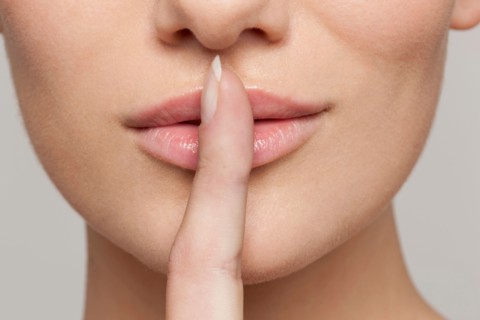 Studio shot portrait of young woman in white blouse with finger on lips