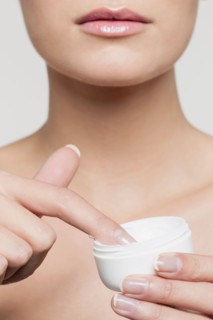 Mid section of young woman applying moisturizer
