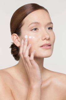 Studio shot of young woman applying moisturizer on face