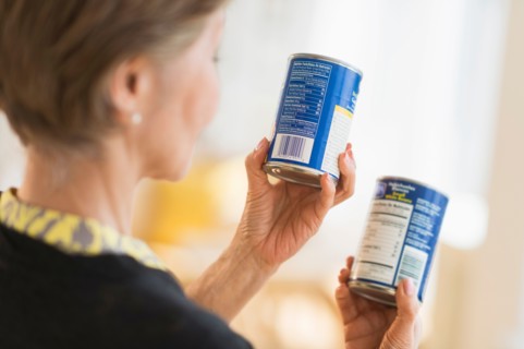 Senior woman reading labels on canned food.