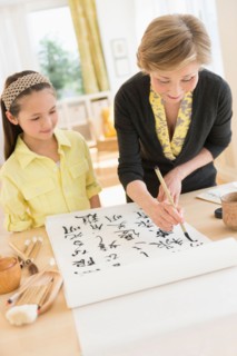 Grandmother and granddaughter (8-9) painting japanese symbols.
