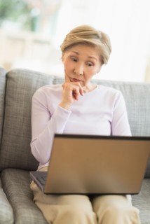 Senior woman sitting on sofa and using laptop.