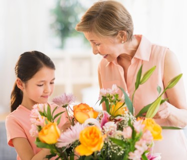 Granddaughter (8-9) and grandmother arranging flowers at home.