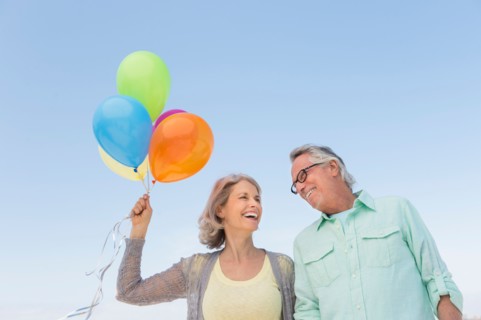 Senior couple with bunch of balloons against clear sky.