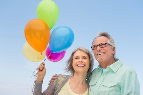 Senior couple with bunch of balloons against clear sky.