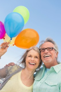 Senior couple with bunch of balloons against clear sky.