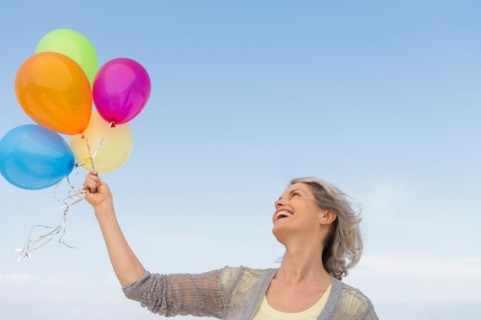 Senior woman holding bunch of colorful balloons.