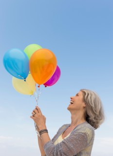 Senior woman holding bunch of colorful balloons.