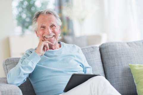 Senior man sitting on sofa with digital tablet.