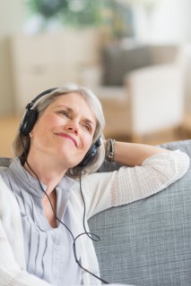 Senior woman sitting on sofa and listening to music.