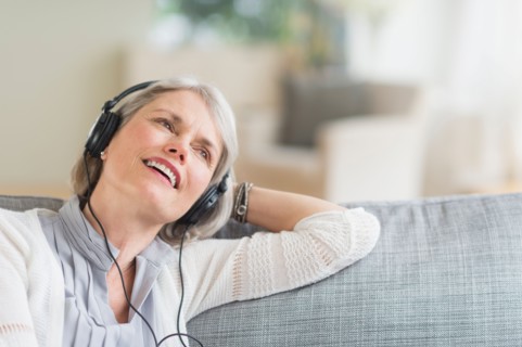Senior woman sitting on sofa and listening to music.