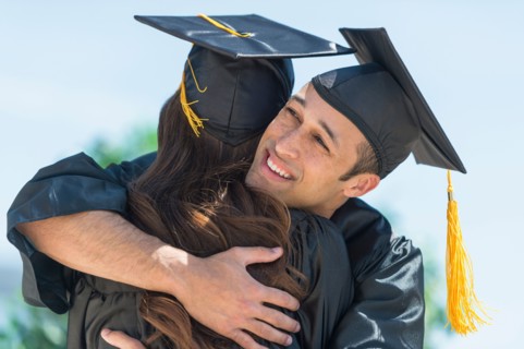 Male and female students embracing on graduation ceremony.
