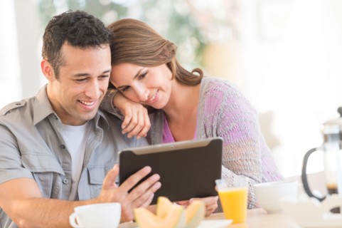 Young couple using digital tablet at kitchen table.