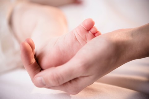 Close up of mother's hand holding tiny foot of baby girl (6-11 months)