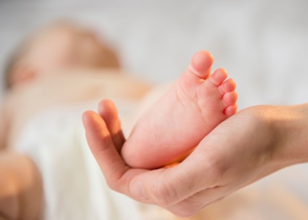 Close up of mother's hand holding tiny foot of baby girl (6-11 months)