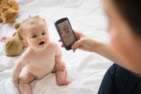 Mother photographing her baby daughter (6-11 months) with mobile phone