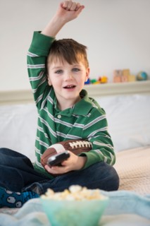 Portrait of cheerful boy (4-5) sitting on bed, holding football