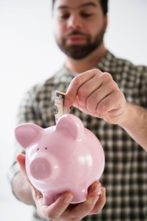 Portrait of man holding piggy ban and putting money inside